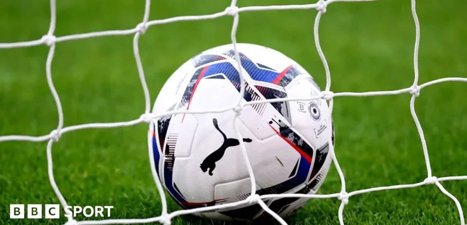 Football resting in goal net on grassy field