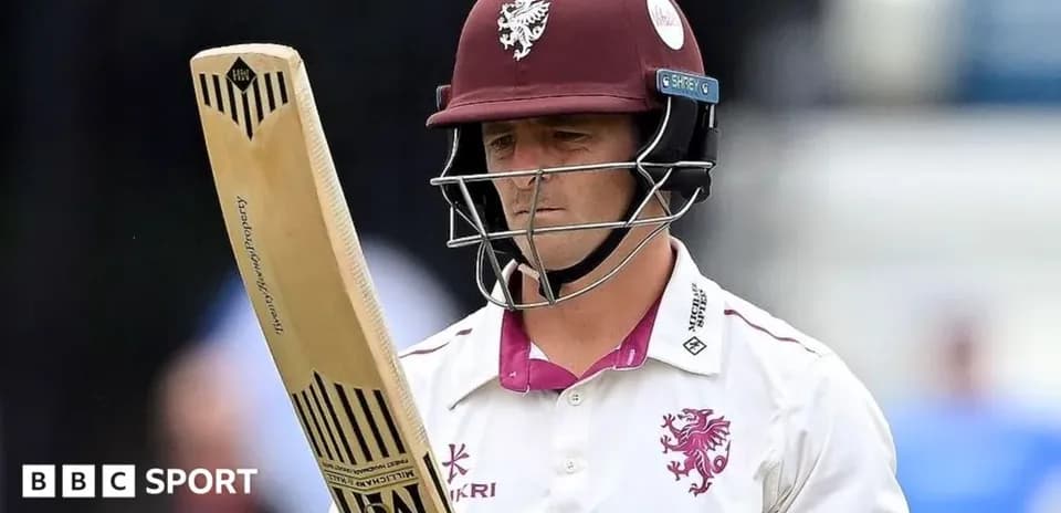 Cricketer holding bat, wearing helmet and team jersey