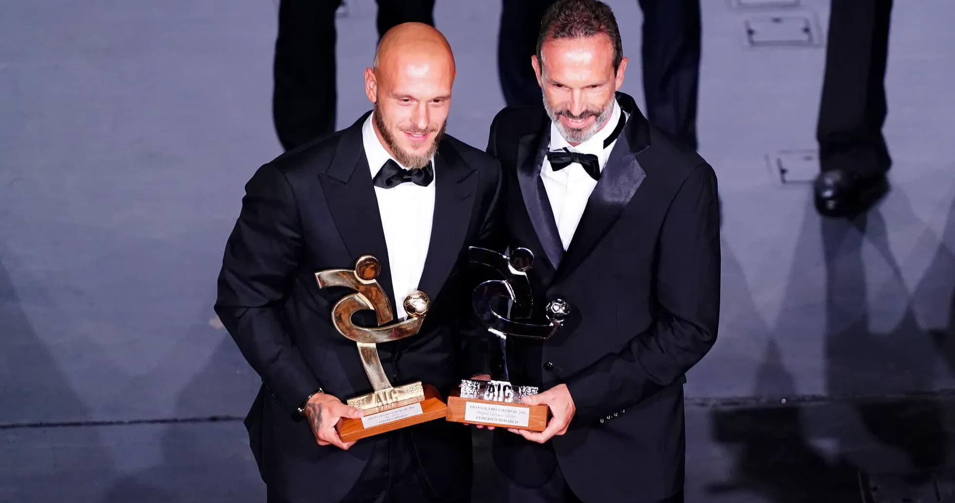 Two men in tuxedos holding awards on stage