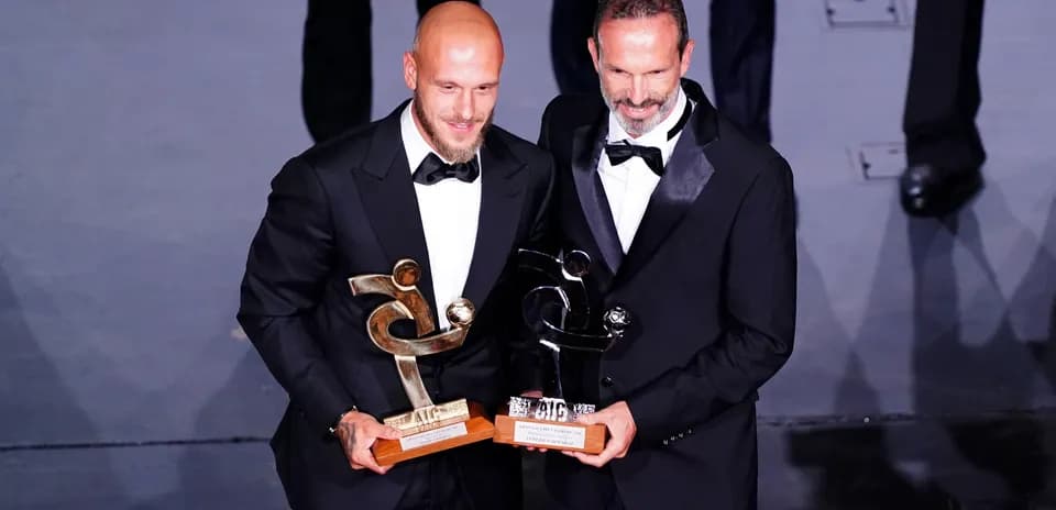 Two men in tuxedos holding awards on stage