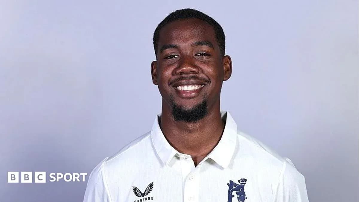 Cricketer smiling in team uniform against plain background