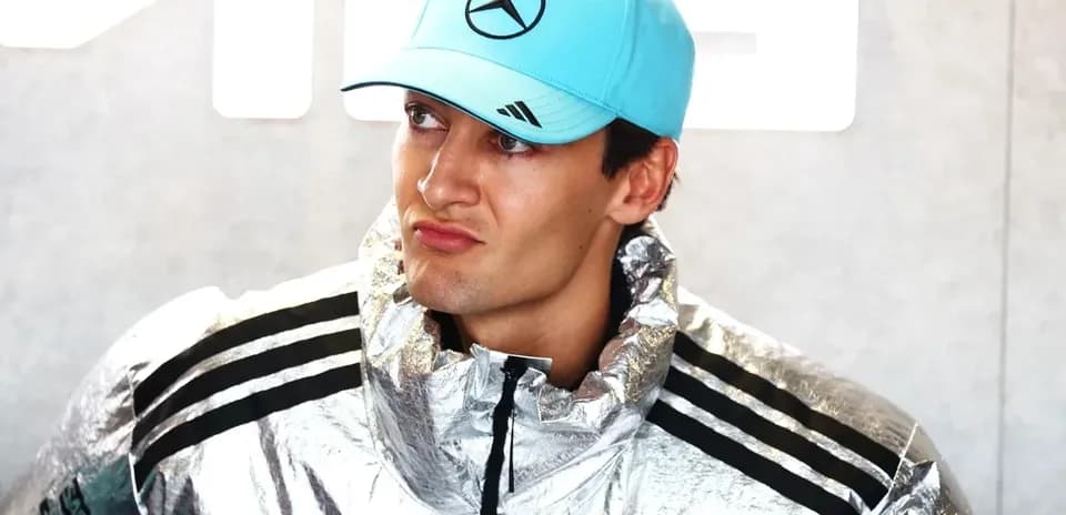 Driver wearing silver jacket and blue cap in paddock
