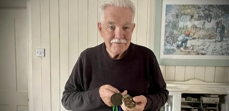 Elderly man holding medals in living room