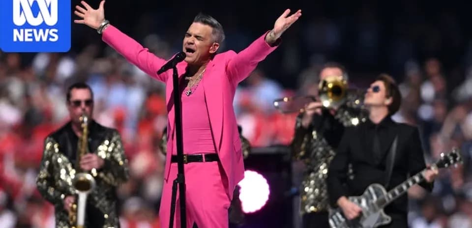 Robbie Williams performing on stage in pink outfit
